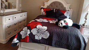 Een bed met een bloemenprint, een zacht knuffelbeest en een witte ladekast.