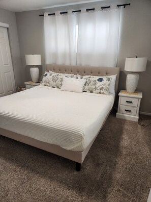 A bedroom with a bed, two nightstands, a window with curtains, and a door. - Amazing Heated Pool & Game Room with 3 bedrooms + converted garage/game room (Sarasota)