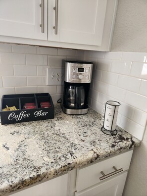 Eine Küche mit Kaffeemaschine, einem Schild mit der Aufschrift ‚Kaffee Bar‘ und einem Mughalter mit motivierenden Sprüchen.