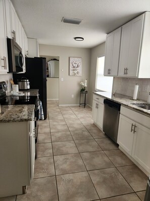 A kitchen with white cabinets, a black refrigerator, a stainless steel stove, and a dishwasher. - Amazing Heated Pool & Game Room with 3 bedrooms + converted garage/game room (Sarasota)