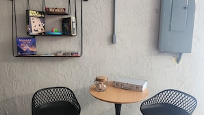 Um quarto com uma mesa redonda, duas cadeiras, uma estante de livros e um aparelho de ar condicionado.
