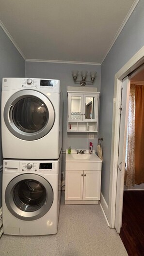 A laundry room with two stacked front-loading washing machines, a white cabinet with a mirror, and a light fixture above. - Cozy Oneonta Getaway (Oneonta)