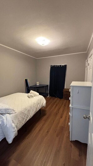 Ein kleines, gut beleuchtetes Schlafzimmer mit einem Einzelbett, einem kleinen Tisch, einem Kleiderschrank und einem Spiegel.