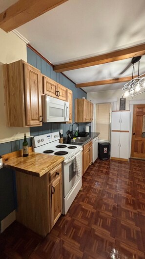 A kitchen with wooden cabinets, a white stove, a microwave, and a sink. - Cozy Oneonta Getaway (Oneonta)