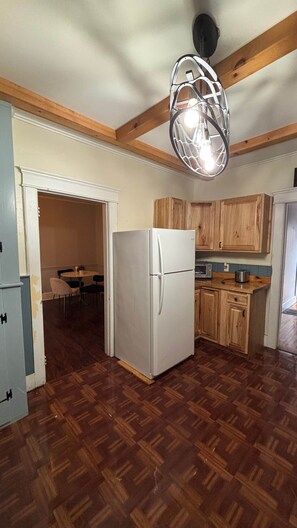 A kitchen with wooden cabinets, a white refrigerator, and a hanging light fixture. - Cozy Oneonta Getaway (Oneonta)