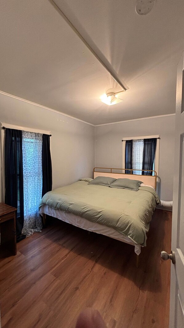 A bedroom with a bed, wooden flooring, a nightstand, and a window with curtains. - Cozy Oneonta Getaway (Oneonta)