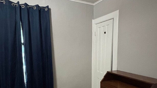 Een kamer met een houten dressoir, een deur en een donker gordijn.