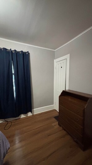 A room with a wooden dresser, a door, and a dark curtain. - Cozy Oneonta Getaway (Oneonta)