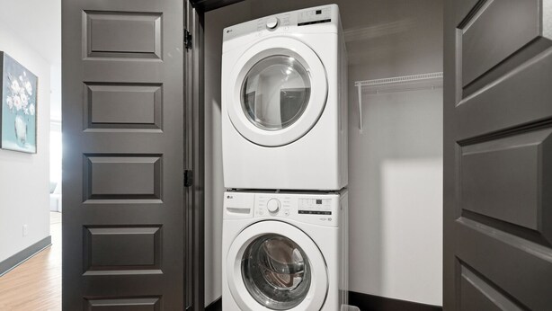 A laundry room with two stacked white washing machines, a wooden floor, and a gray door. - Modern Emerald Oasis 
Stylish Decatur Getaway (Decatur)