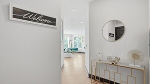 A hallway with a 'Welcome' sign, a round mirror, and a console table with decorative items. - Modern Emerald Oasis 
Stylish Decatur Getaway (Decatur)