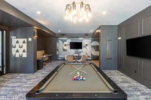 A pool table with balls, a television, and seating in a modern room with grey walls and a patterned carpet.