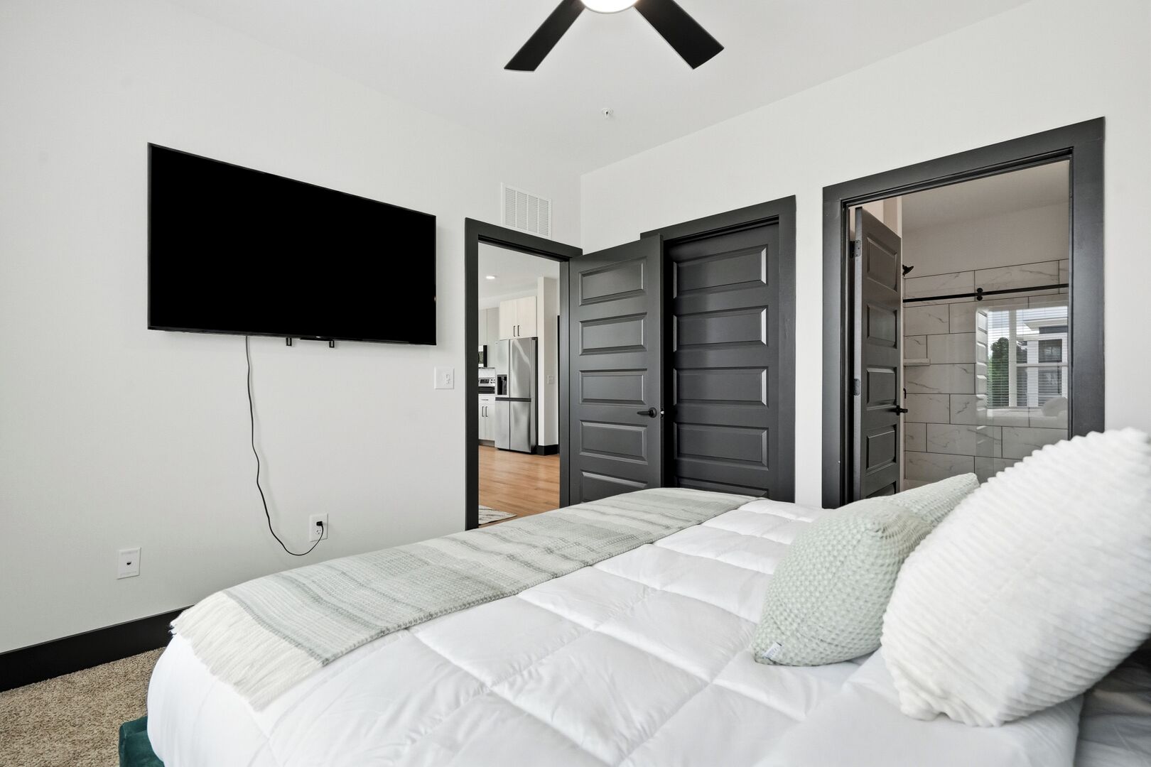 Une chambre à coucher avec un lit, un téléviseur fixé au mur et une porte donnant sur une salle de bain.