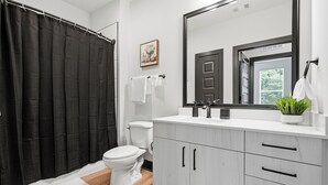A modern bathroom with a shower curtain, toilet, sink, mirror, and cabinets. - Modern Emerald Oasis 
Stylish Decatur Getaway (Decatur)