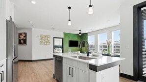 A modern kitchen with a central island, stainless steel appliances, and a green accent wall. - Modern Emerald Oasis 
Stylish Decatur Getaway (Decatur)