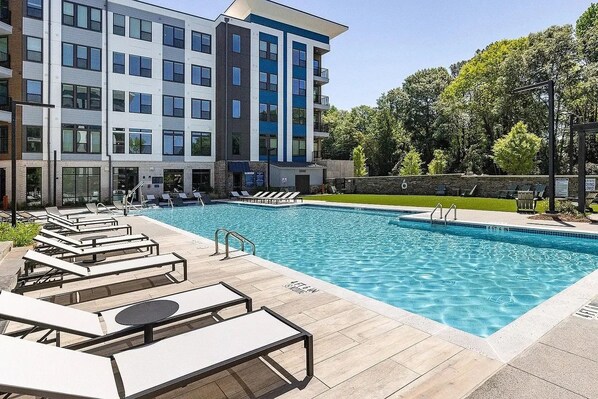 A modern building with a swimming pool, lounge chairs, and a stone wall.