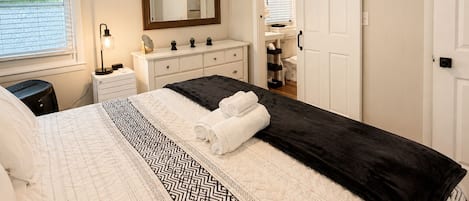 A bedroom with a bed, a dresser, a mirror, a ceiling fan, and a sliding door to a bathroom.