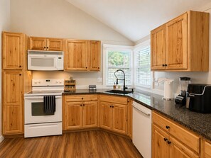 Una cocina con armarios de madera, una estufa blanca, microondas, un lavamanos y una cafetera.