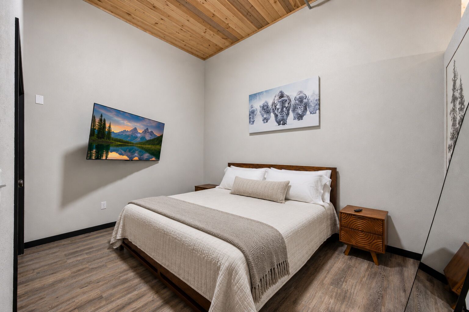 A bedroom with a bed, a nightstand, a wooden headboard, and two wall-mounted paintings.