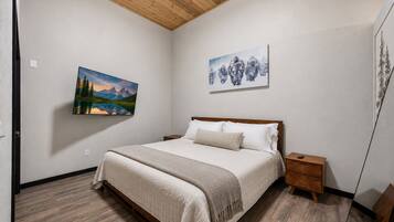 A bedroom with a bed, a nightstand, a wooden headboard, and two wall-mounted paintings.