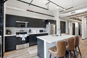 A modern kitchen with dark cabinets, stainless steel appliances, and a central island with bar stools.