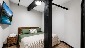 Una camera da letto con un letto, una TV, un comodino in legno e un quadro appeso al muro.