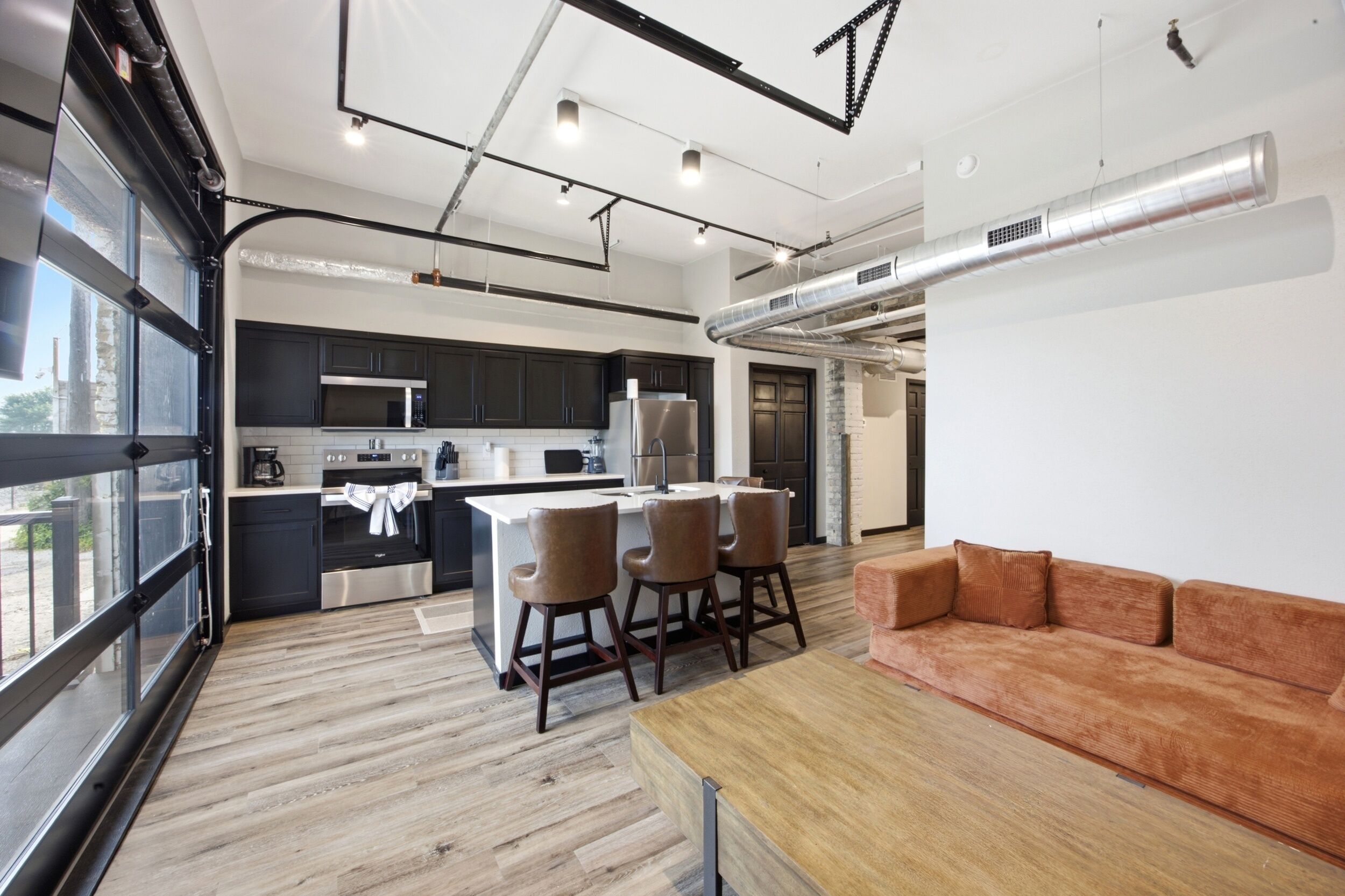 A modern kitchen with dark cabinets, stainless steel appliances, and a central island with bar stools.