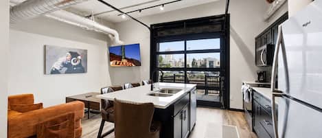 A modern kitchen with a large island, stainless steel appliances, and a city view through a large window.