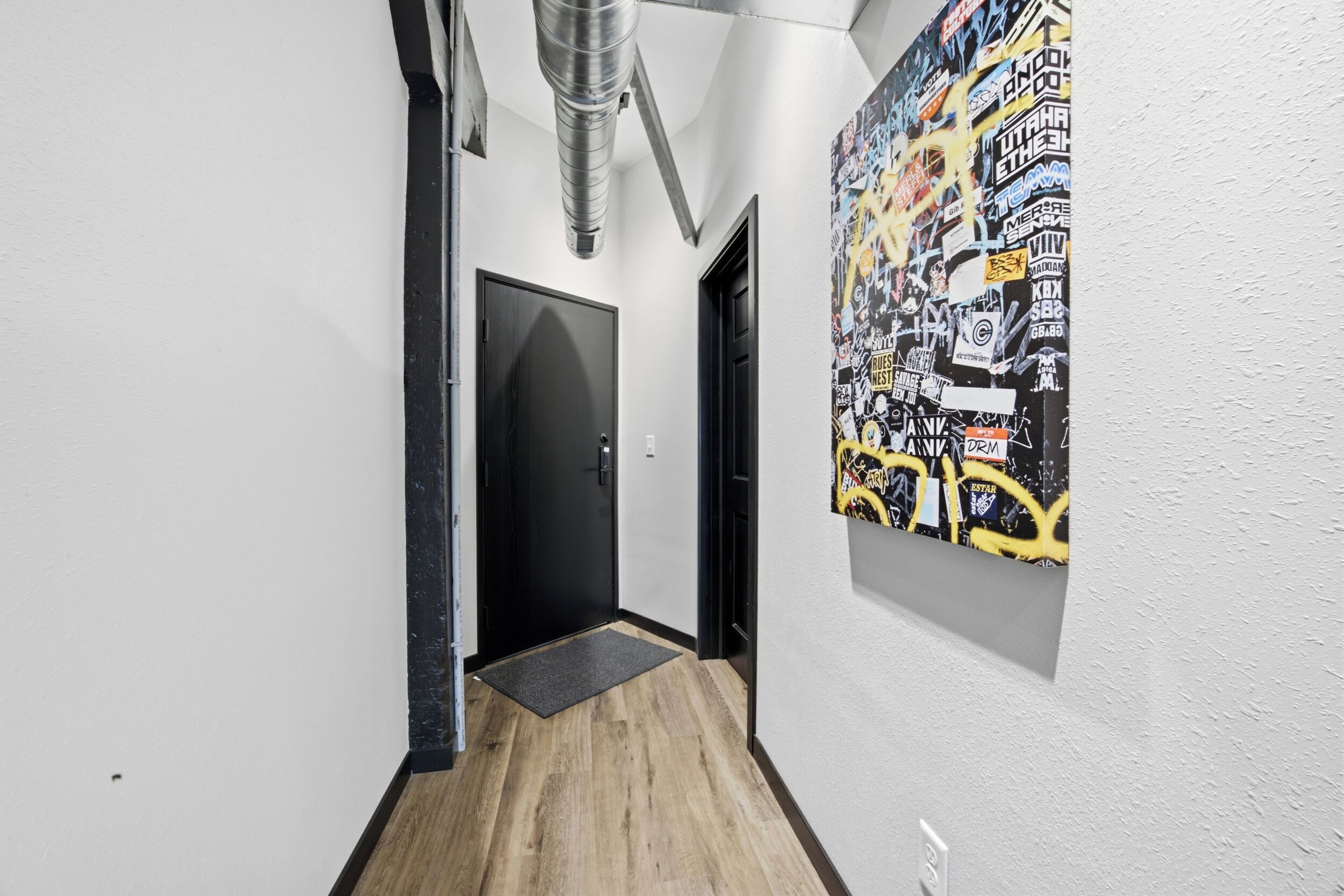 A hallway with a black door, a doormat, and a wall with a graffiti-style poster.