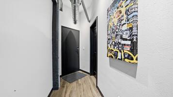 A hallway with a black door, a doormat, and a wall with a graffiti-style poster.