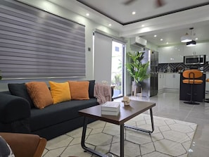 A modern living room with a sofa, coffee table, and a view into the kitchen. - Boutique Styled 2BR Luxury Retreat Where Modern Comfort Meets a Relaxing Escape (Runaway Bay)