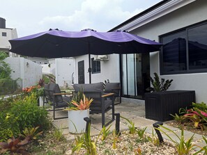 Ein Patio-Bereich mit Gartenmöbeln, einem großen Sonnenschirm und Kübelpflanzen.
