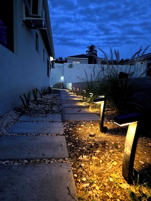 A pathway leading to a building with a white exterior, surrounded by gravel and plants. - Boutique Styled 2BR Luxury Retreat Where Modern Comfort Meets a Relaxing Escape (Runaway Bay)