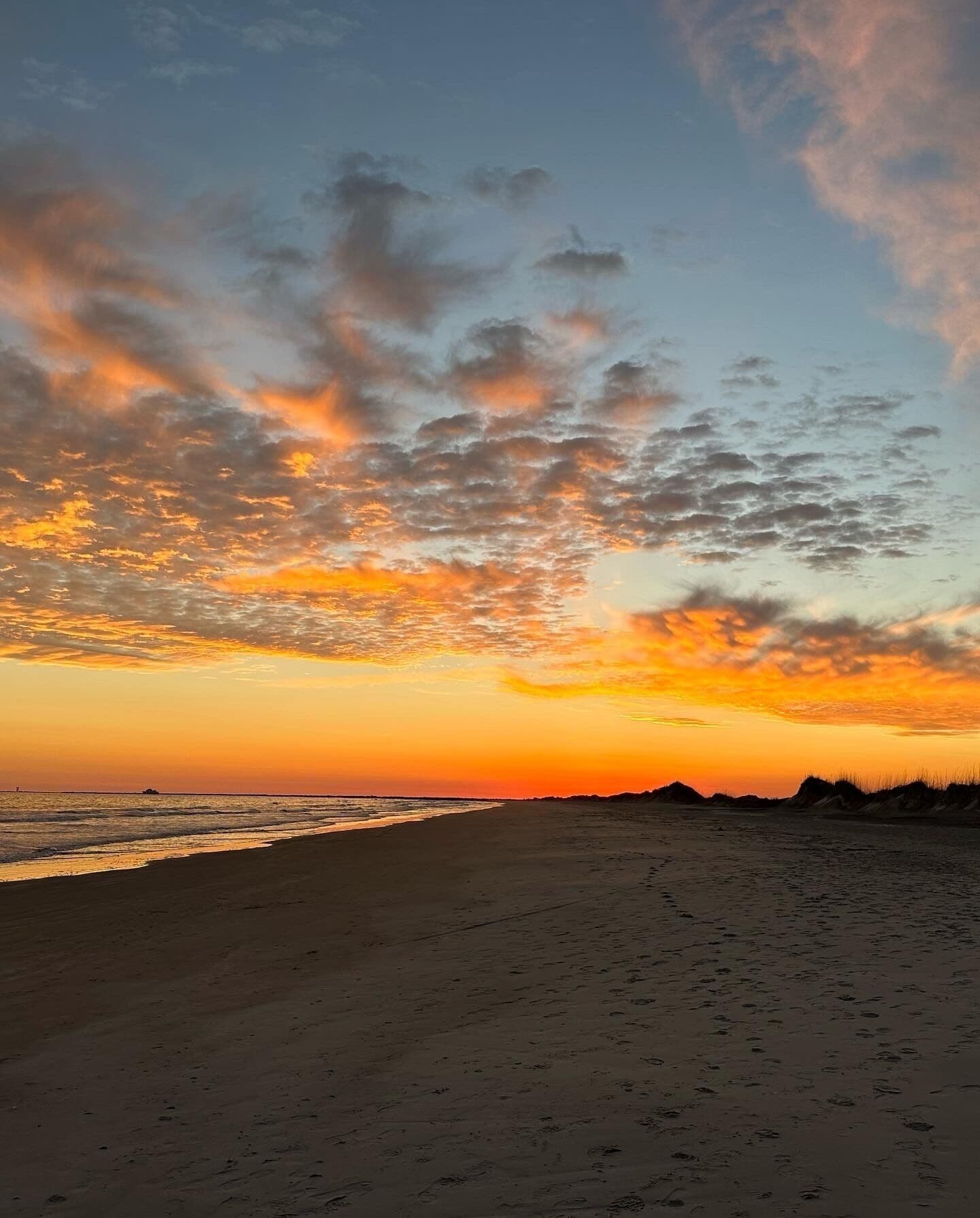 Une plage dotée d’un large rivage sablonneux et d’un ciel dégagé parsemé de nuages.