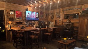 A bar area with wooden decor, a television displaying a movie, and a cowhide rug on the floor. - Perfect 2-bedroom cabin in soothing Custer for a relaxing stay. (Custer)