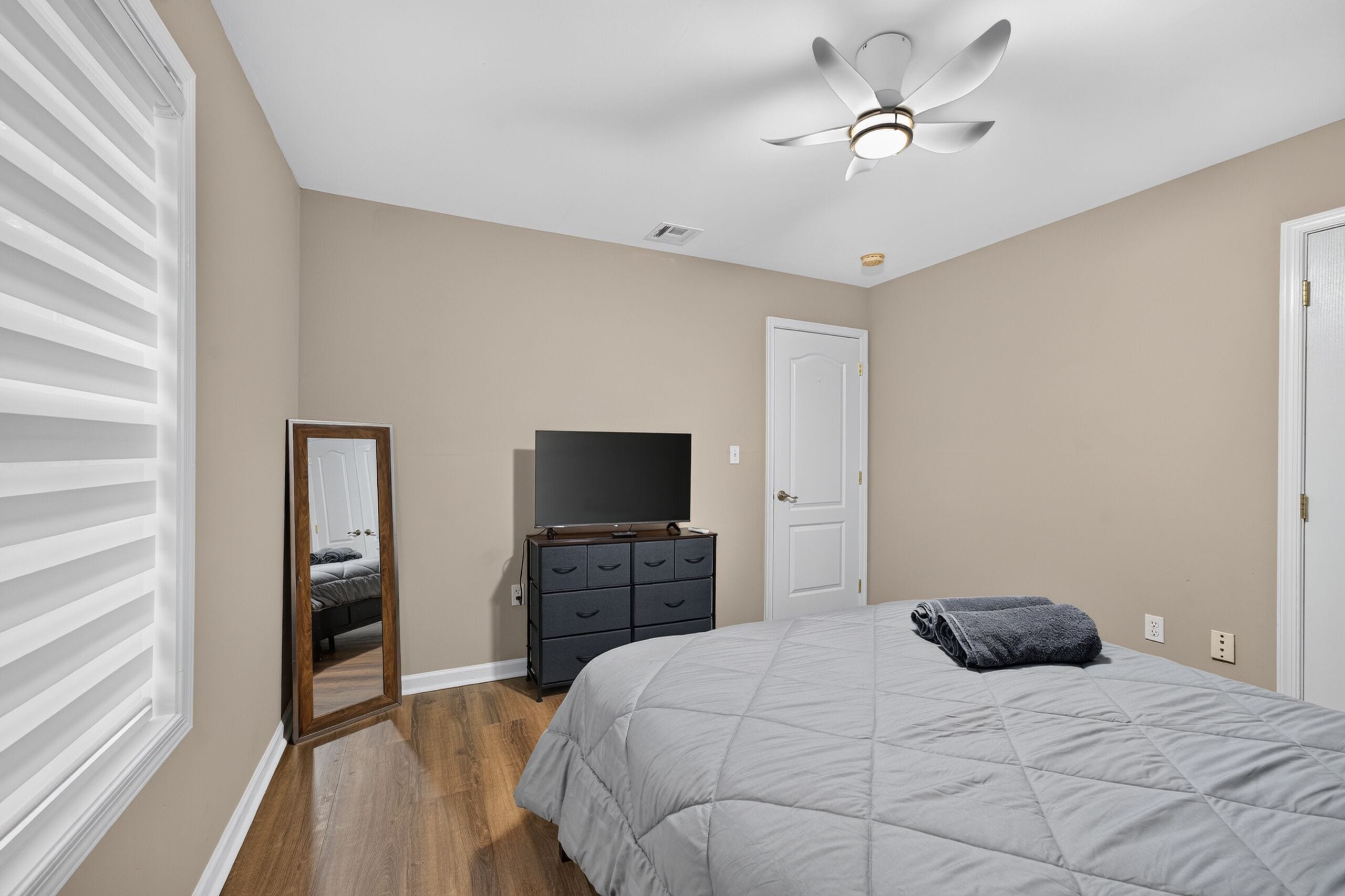 Ein Schlafzimmer mit Bett, Kommode, Fernseher, Deckenventilator und einer Tür.