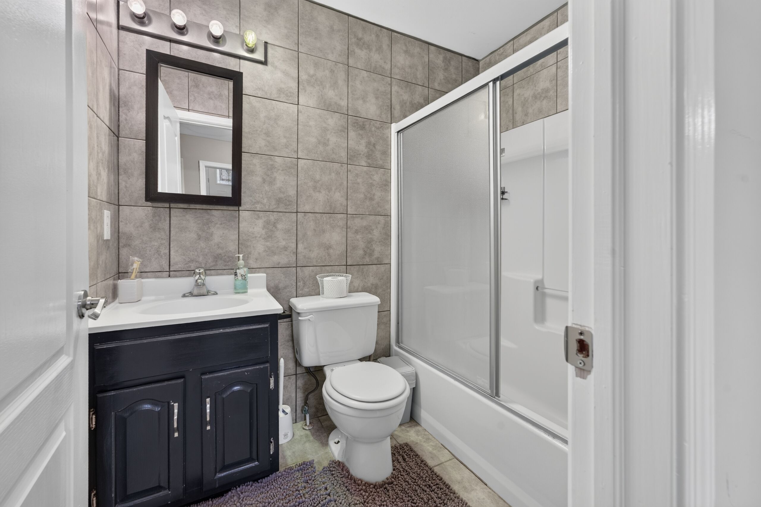 Un baño con lavamanos blanco, muebles oscuros, inodoro y zona de ducha.