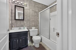 Un baño con lavamanos blanco, muebles oscuros, inodoro y zona de ducha.