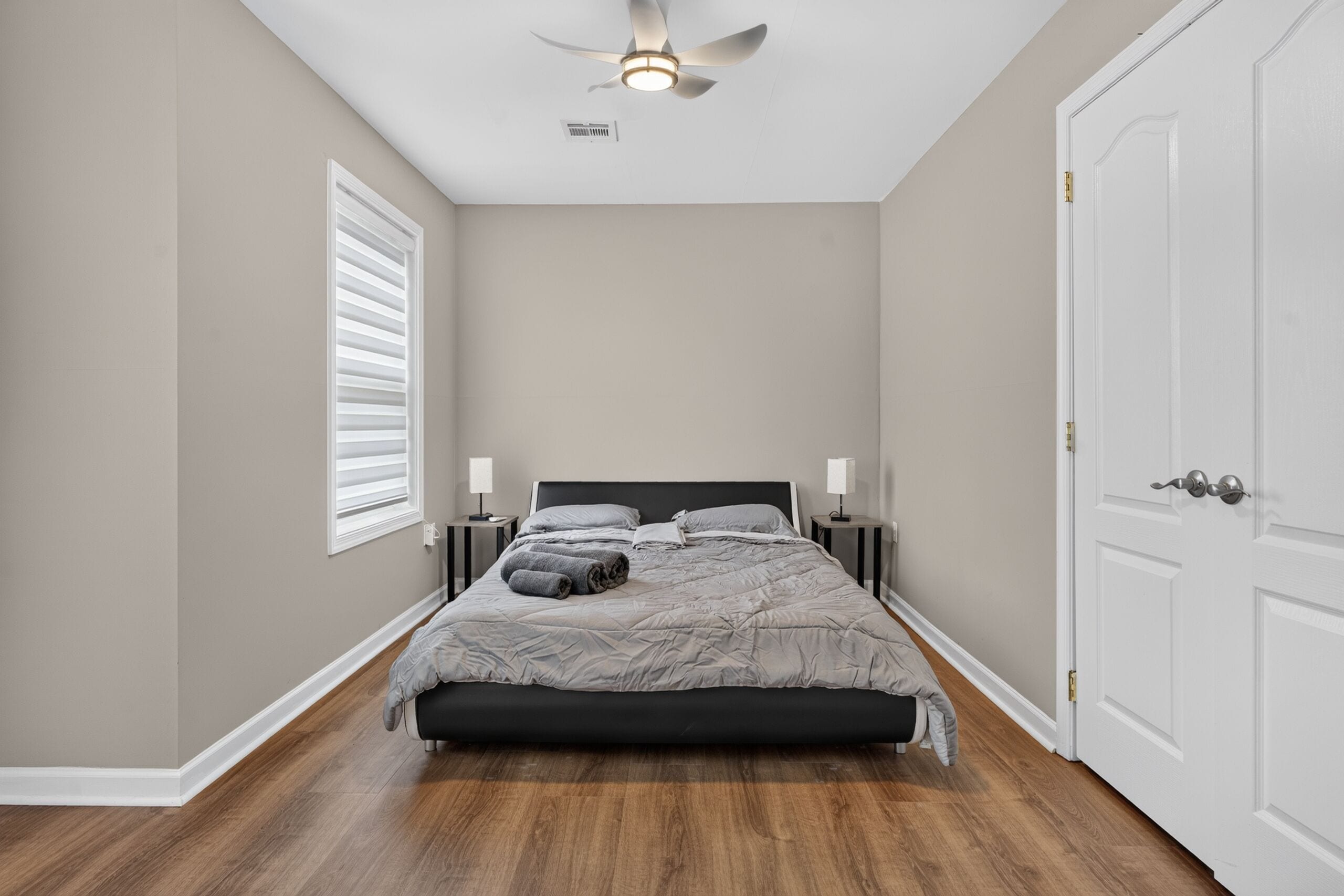 Un dormitorio con cama, mesitas de noche, ventilador de techo y una puerta.