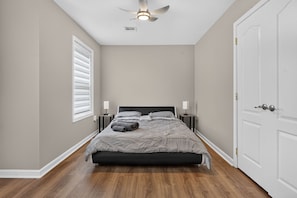 Un dormitorio con cama, mesitas de noche, ventilador de techo y una puerta.