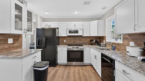 A modern kitchen with white cabinets, a stainless steel refrigerator, a built-in microwave, and a granite countertop.