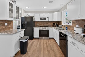 Cocina moderna con armarios blancos, refrigerador de acero inoxidable, microondas integrado y encimera de granito.