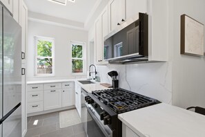 Eine moderne Küche mit weißen Schränken, einem Gasherd und einem großen Fenster für natürliches Licht.