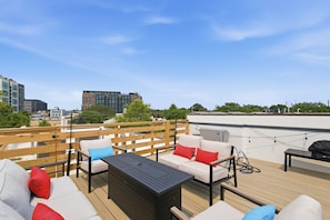 Eine Dachterrasse mit Gartenmöbeln, einem Grill und Blick auf Stadtgebäude.