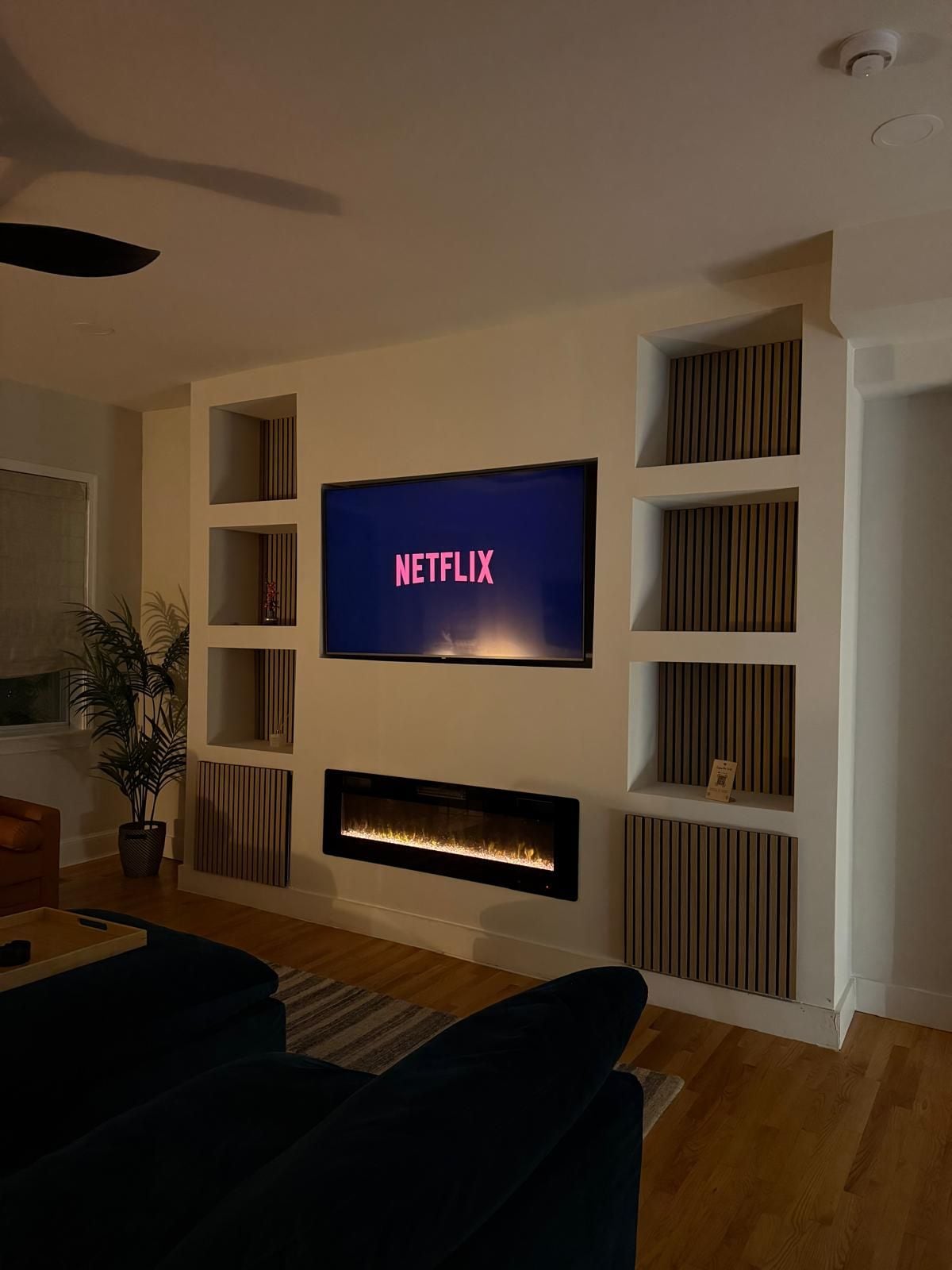 Ein modernes Wohnzimmer mit einem an der Wand befestigten Flachbildfernseher, einem integrierten Kamin und einem Bücherregal mit dekorativen Gegenständen.