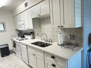 A modern kitchen with white cabinets, stainless steel appliances, and a patterned backsplash. - Ground level condo with a large enclosed patio, steps from the pool (Palm Springs)
