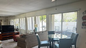 A living room with a TV, sofa, and a dining area with chairs and a table. - Ground level condo with a large enclosed patio, steps from the pool (Palm Springs)
