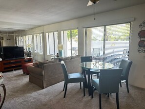 Ein Wohnzimmer mit Fernseher, einer Couch und einem Essbereich mit Stühlen und Tisch.