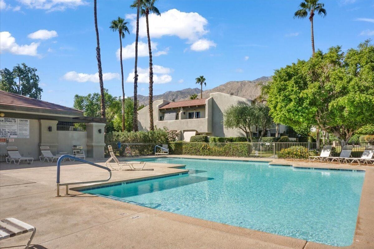 A swimming pool with lounge chairs, palm trees, and a building with a red roof.