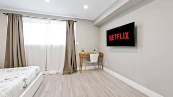 Une chambre à coucher moderne, avec un lit, un bureau, une chaise, un téléviseur fixé au mur et une fenêtre avec des rideaux.