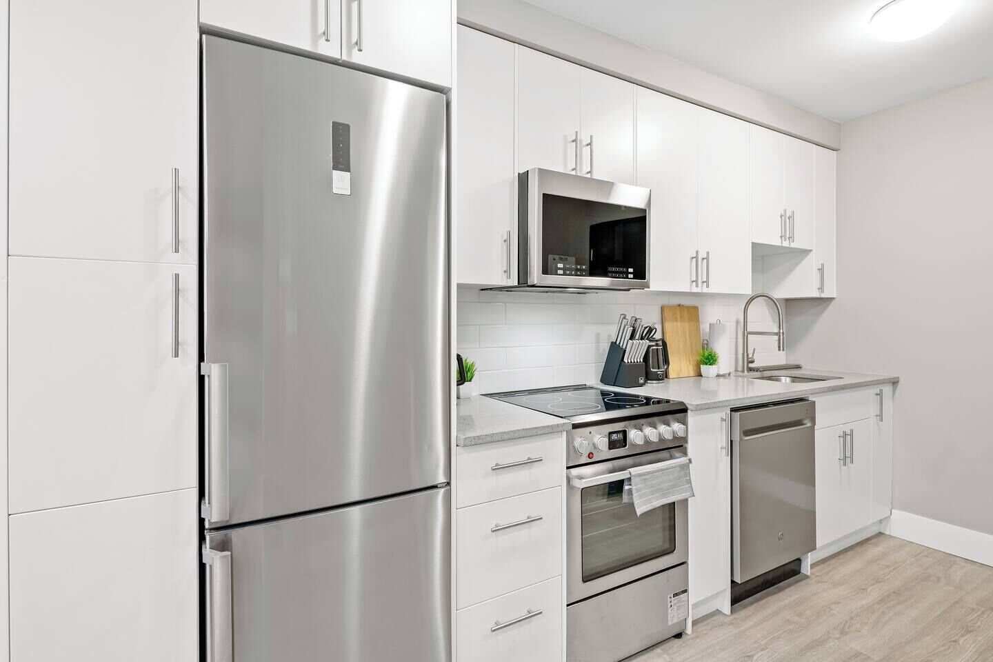 A modern kitchen with stainless steel appliances, white cabinetry, and a built-in microwave.